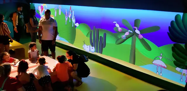 Crianças pintando diante da parede mapeada com o cenário de Tarsila